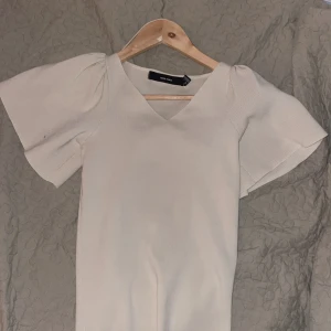 Vit kortklänning med v-ringning Vero Moda - Supersöt vit kortklänning från Vero Moda i storlek XS. Klänningen har en snygg v-ringad hals och puffiga korta ärmar som ger en trendig look. Materialet är mjukt och stickat, perfekt för dig som gillar stilrena och ljusa plagg.