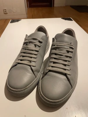 Axel Arigato skor 42 passar 43 - Snygga grå sneakers från Axel Arigato med stilren design och rund tå. Skorna är tillverkade i slätt skinn med matchande grå snörning och har en platt sula. Bakkappan har en kontrasterande mockadetalj som ger extra edge till looken. Använda 3 till 4 gånger.