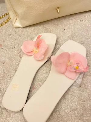 Vita sandaler med rosa blommor - Superfina vita sandaler med fyrkantig tå och transparent rem, dekorerade med stora rosa blommor framtill. Perfekta för dig som vill sticka ut med en söt och trendig detalj. Lätta att matcha till somriga outfits.
