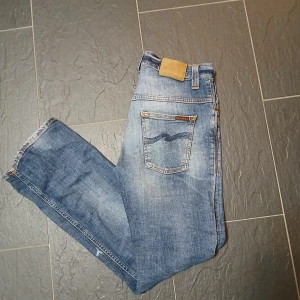 Nudie - Snygga blå jeans med tapered passform och klassisk femficksdesign. Jeansen har en mörk tvätt med lätt slitning och kontrastsömmar. Slim fit. Nudie thinn finn, Storlek 32