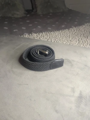 Svart flätat bälte med silverfärgat spänne Jack & Jones - Snyggt svart bälte med flätad design och silverfärgat metallspänne. Bältet har detaljer i svart skinn vid spännet och änden, vilket ger en stilren och modern look. Perfekt accessoar för att lyfta din outfit.