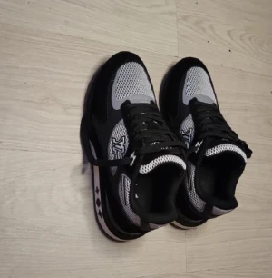 Svarta och vita sneakers - Skriv om ni vill ha bild på lådan. Snygga sneakers i svart och vitt med reflekterande detaljer. Skorna har logga på sidan och plösen, mesh- och mockapartier samt snörning. Sulan har coola stjärndetaljer och skorna har en sportig vibe som sticker ut.