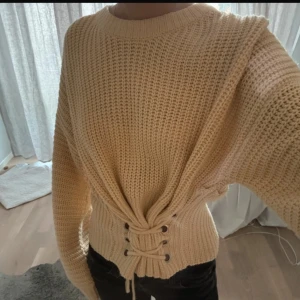Beige stickad tröja med snörning - Säljer en cremevit/beige stickad tröja med snörning i midjan. Skulle säga att den passsr en S/M beroende på hur man knyter den