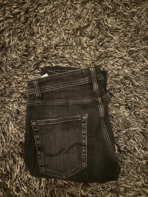 Svarta jeans från Jack & Jones, 29/30 - Snygga svarta jeans från Jack & Jones med klassisk femficksdesign och diskreta slitningar. Modellen har raka ben och normal passform, perfekt för dig som gillar stilrena och enkla jeans. Materialet är mjukt denim och midjan är midwaist.
