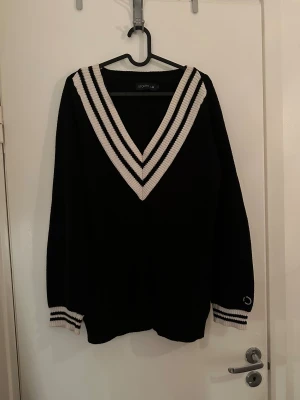 Svart stickad v-ringad tröja Stockh LM - Svart stickad tröja från Stockh LM med bred v-ringning och vita samt svarta ränder längs halsen och ärmsluten. Är större i Stl och mer som M/L
