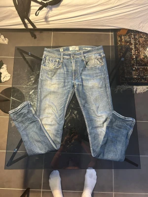 Replay Anbass ljusblå jeans 29/32 - Säljer ett par Replay Anbass jeans i ljusblå tvätt med klassisk femficksdesign och snygga slitningar. Jeansen har rak passform, normal midja och är tillverkade i mjukt bomullsmaterial med lite stretch. 