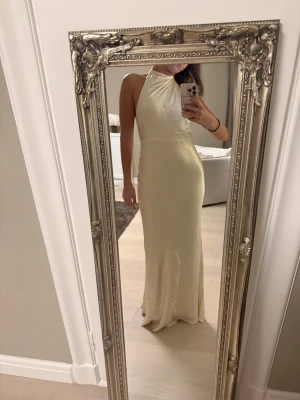 Ljusgul långklänning från meshki  - Säljer en elegant ljusgul långklänning med halterneck och öppen rygg i satin. Använd en gång men har inga tecken på användning.