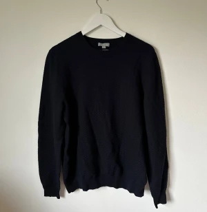 Mörkblå strukturerad tröja från COS - Mörkblå långärmad tröja från COS i storlek L. Tröjan har en snygg strukturerad yta och är tillverkad i 100% bomull. Rund halsringning och ribbade muddar vid ärmslut och nederkant ger en clean look. Perfekt för dig som gillar minimalistisk stil. 4Ä10