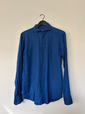 Blå skjorta från Eton - Snygg blå skjorta från Eton med klassisk krage och svarta knappar hela vägen. 52 % bomull, 48 % Polyamid