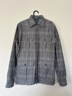 Grå rutig overshirt från Eton - Snygg grå overshirt från Eton i rutig design. Jackan har klassisk krage, fyra stora fickor framtill med knappar och är tillverkad i mjukt ullmaterial. Perfekt lager-på-lager-plagg med stilren vibe och lång ärm. NYPRIS: Cirka 5000 kr 