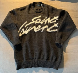 Saint Laurent mohair tröja - Svart stickad mohair tröja från Saint Laurent med vit, fluffig logotyp framtill. Tröjan har rund hals, ribbade muddar och långärmad passform. Sjukt snygg och elegant som också värmer bra under vintern. Storlek M. Använd cirka en gång. Bara att höra av dig om du har någon fundering! :)