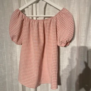 Rutig rosa röd offshoulder blus - Säljer en söt rosa och vit rutig blus med offshoulder och puffiga korta ärmar. Blusen har en luftig passform. Jättesöt att ha under en kofta. Hör av dig vid frågor 🩷