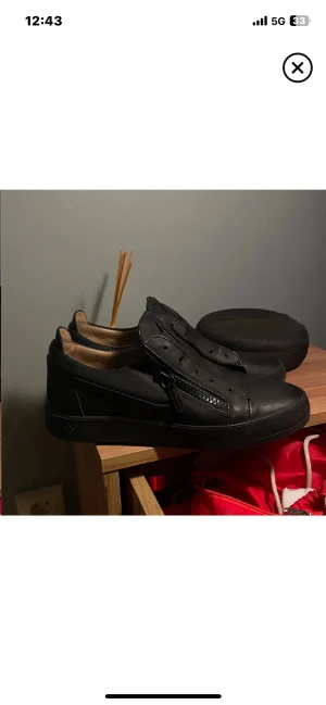 Svarta sneakers från Giuseppe Zanotti - Säljer ett par svarta sneakers från Giuseppe Zanotti i skinn med dragkedjor på sidorna och signaturlogga på plösen. Skorna har rund tå, platt sula och stilren design som passar till många outfits. Riktigt snygga och exklusiva sneakers för dig som gillar streetstyle.