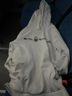 Vit hoodie från Sail Racing      pruta på!! - Vit hoodie från Sail Racing med svart logga på bröstet och broderad detalj på huvan. Klassisk känguruficka framtill och skön passform. Tillverkad i mjuk bomulls- och polyestermix som känns riktigt nice mot huden.