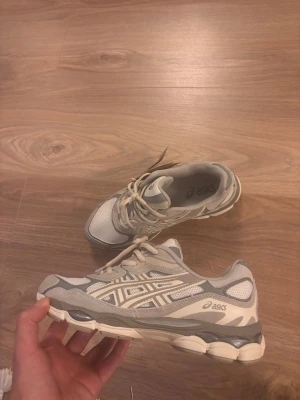Gråvita Asics sneakers med mesh och mocka - Säljer ett par snygga Asics sneakers i grått och vitt med klassisk logga på sidan. Skorna har meshpaneler för bra andningsförmåga och detaljer i mocka och syntet. Sulan är chunky och ger en sportig vibe. Perfekta för dig som gillar stilrena och bekväma sneakers.