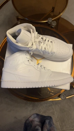 Air jordan 1 Mid  - Nike Jordan 1 Mid white  sneakers med clean och stilren design. Helt vita med snörning, perforerad tå och klassisk Jordan-logga på sidan. Skorna har en hög siluett och är tillverkade i skinn med platt sula och rund tå. Perfekta för dig som gillar minimalistisk streetstyle.Skorna är i mycket fint skick utan märken, eftersom jag bara har använt dem vid ett tillfälle.