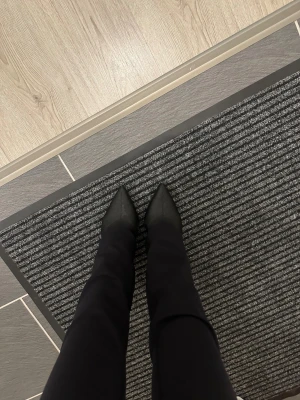 Svarta stövletter med klack - Säljer ett par svarta stövletter med spetsig tå och hög klack. Snygg, smal siluett som sitter tight runt foten och ankeln. Materialet ser ut att vara syntet eller skinn, och färgen är helsvart. Perfekt för dig som gillar stilrena och trendiga boots.