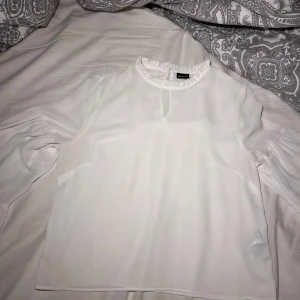 Vit blus med volang från Gina Tricot - Säljer en vit blus från Gina Tricot i storlek 36. Blusen har rund hals med söt volangkant och långa ärmar med lätt puff och rynk vid axlarna. Små fläckar vid slutet av armen, se sista bild🩷