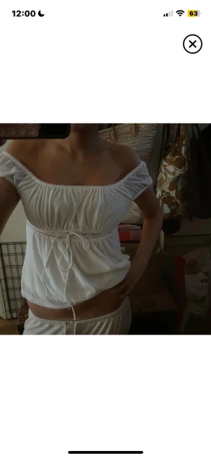 Vit omlott blus med snörning - Säljer en oanvänd vit blus med omlottkänsla och snörning i midjan. Toppen har offshoulder men man kan även ha den lite som man vill, toppen har puffiga korta ärmar, samt spetsdetaljer längs halsringningen. Materialet är lätt och luftigt, perfekt för varma dagar. Söt och romantisk vibe!