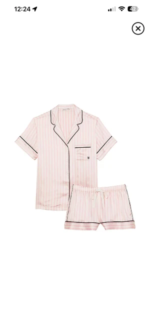 Randiga pyjamasshorts i rosa och vitt - Säljer ett par söta pyjamasshorts i ljusrosa och vitt med vertikala ränder. Shortsen har svart kantband och snörning i midjan för extra komfort. Perfekta för mysiga hemmakvällar.