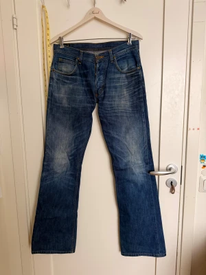 Blå bootcut jeans från Lee - Snygga blå jeans från Lee med klassisk bootcut-passform och fem fickor. Jeansen har slitningar och kontrastsömmar, samt Lee-logga på bakfickan och läderpatch i midjan. Perfekta för dig som gillar retrovibe och bredare ben.