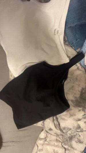 Ribbade linne-toppar från Zara & Gina Tricot - Två ribbade linne-toppar, en vit från Zara i storlek 152 och en svart från Gina Tricot i XXS. Båda har en ärmlös, croppad passform med rund halsringning och stretchigt material. Perfekta att matcha med jeans eller kjol för en clean look.