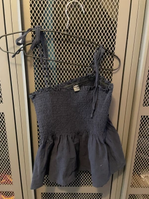 Mörkblå linnetopp från SHEIN - Supersöt mörkblå linnetopp från SHEIN med smockad överdel och volang nertill. Toppen har tunna axelband som knyts på axlarna för en extra gullig touch. Perfekt för varma dagar och enkel att styla med jeans eller kjol.