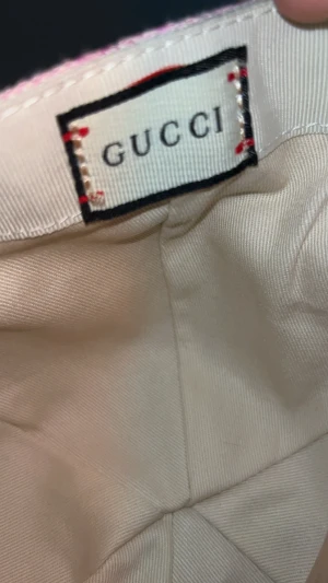 Rosa Gucci keps med GG-mönster - Säljer en snygg rosa keps från Gucci med ikoniskt GG-monogram över hela kepsen. Kepsen har böjd skärm, justerbart spänne bak i rosa och är tillverkad i bomullsmix med detaljer i läder. Perfekt för dig som vill sticka ut med lyxig streetstyle.