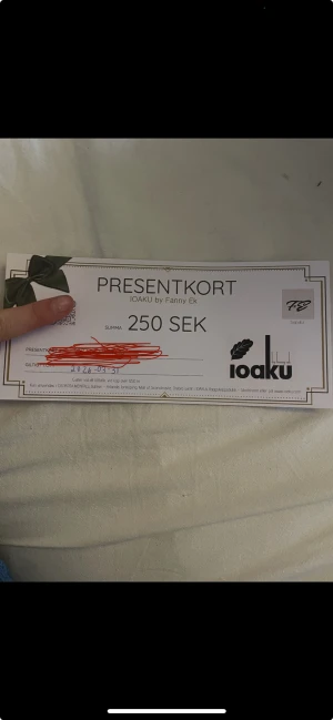 Presentkort IOAKU by Fanny Ek 250 kr - Presentkort på 250 SEK till IOAKU by Fanny Ek, perfekt för att köpa smycken som ringar, armband, halsband eller örhängen. Giltigt till 2026-03-31 och kan användas i flera butiker och online. Snygg design med grön rosett och IOAKU-logga. OBS! Gäller bara om man handlat för 1250kr! Endast öppnad för att ta kort!