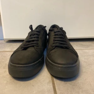 Svarta sneakers från Vagabond - Snygga helsvarta sneakers från Vagabond med rund tå och platt sula. Skorna har klassisk snörning och är tillverkade i mocka med insida i skinn. Perfekt för dig som gillar stilrena och minimalistiska skor med en urban vibe.