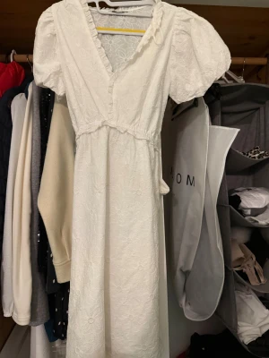 Vit  klänning med puffärm - Superfin vit klänning,puffärmar och v-ringning. Klänningen har knytband i midjan och volangdetaljer vid halsen. Perfekt för sommarens alla tillfällen och ger en romantisk vibe.