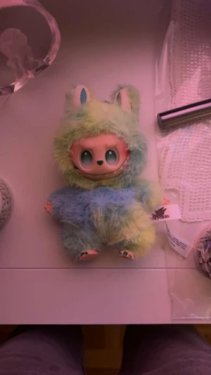 Färgglad fluffig handväska The Monsters - Supergullig handväska från The Monsters i form av ett mjukt, fluffigt djur med stora ögon. Väskan har pastelliga färger i blått, grönt och gult och är tillverkad i syntetpäls. Perfekt accessoar för dig som vill sticka ut med något unikt och lekfullt.