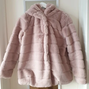 Rosa pälsjacka från Gold & Silver - Mysig rosa pälsjacka från Gold & Silver i syntetmaterial. Jackan har en fluffig huva och långa ärmar, perfekt för kyliga dagar. Den är tillverkad i 100% polyester och har en stilren design med horisontella ränder. Passar storlek S-M. 