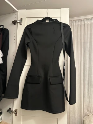 Svart kort klänning - Heiress - Svart kort klänning från Heiress med långärmade, figurnära ärmar och markerad midja. Med prislapp på!