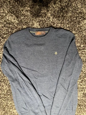 Blå stickad tröja från Morris XS - Snygg mörkblå stickad tröja från Morris i 100% merinoull. Klassisk rund hals och diskret broderad logga på bröstet. Perfekt för dig som gillar stilrena och bekväma plagg med premiumkänsla. 1599kr nypris* 