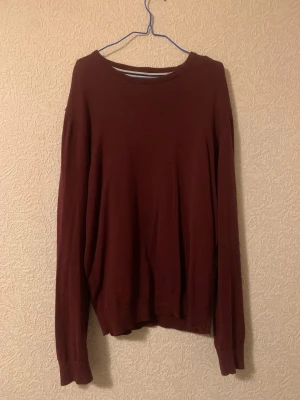 Vinröd tröja från Pier One - Snygg vinröd stickad tröja från Pier One med rund hals och ribbade muddar. Enkel och stilren design som funkar till många olika looks. Materialet är mjukt och känns skönt mot huden. Perfekt för dig som gillar klassiska färger och en clean vibe. 