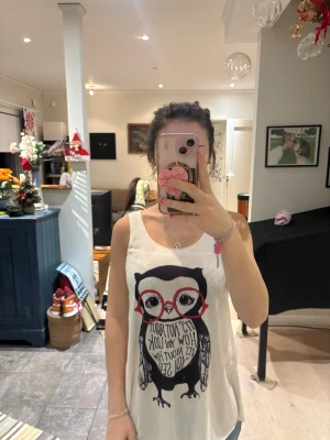 Vit linnetopp med uggletryck - Säljer en vit ärmlös linnetopp med ett stort tryck av en söt uggla med röda glasögon och texten 'It's not about how you look, it's about how you see!' på magen.