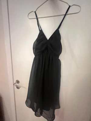 Svart kort klänning Jeane Blush XS - Supersöt svart klänning från Jeane Blush i storlek XS. Klänningen har tunna axelband, v-ringning och ett lätt, flowy tyg som ger en smickrande siluett. 