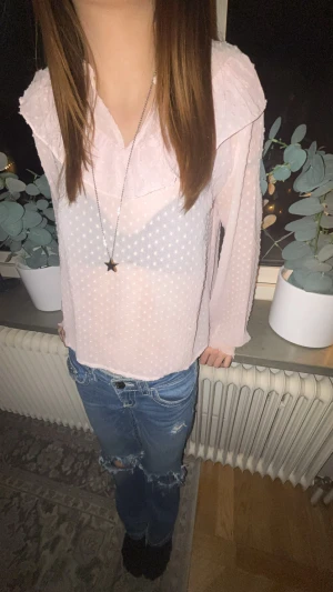 Ljusrosa prickig blus från Gina Tricot - Supersöt ljusrosa blus från Gina Tricot med prickigt mönster och volangdetaljer vid halsen. Blusen har långärmade ärmar med smock vid mudden och är tillverkad i ett lätt och luftigt syntetmaterial. Perfekt för dig som gillar romantiska och trendiga vibes.