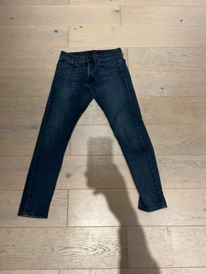 Mörkblå slim jeans från Polo Ralph Lauren - Snygga mörkblå jeans från Polo Ralph Lauren med klassisk femficksdesign och smal passform. Jeansen har en diskret tvätt och silverfärgad knapp med logga. Perfekta för dig som gillar stilrena och tidlösa jeans med en modern touch.