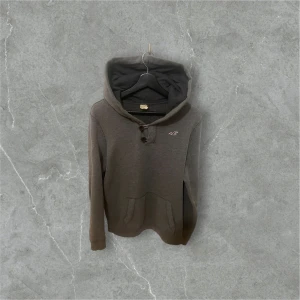Grå hoodie från Hollister med knappar - Säljer en grå hoodie från Hollister i storlek S. Tröjan har huva, två knappar vid halsen och en magficka framtill.