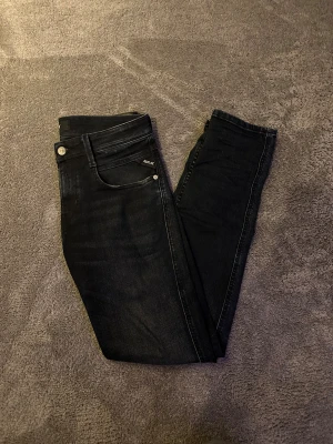 Mörkblå/svarta Replay Anbass jeans W27 L32 - Snygga svarta Replay Anbass jeans i stretchigt material med klassisk femficksdesign och diskreta slitningar. Modellen har smal passform och raka ben, perfekt för en stilren look. Tillverkade i bomullsmix med organisk bomull.
