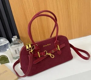 Miu Miu handväska i mocka med gulddetaljer - Snygg handväska från Miu Miu i mocka med guldfärgade metalldetaljer och dubbla dragkedjor. Finns i vinröd, beige, svart och mörkbrun. Väskan har rundad form, dekorativt spänne framtill och både handtag och axelrem i matchande färg.