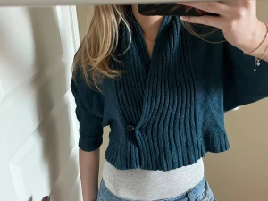 Mörkblå omlott kofta från Vero Moda - Säljer en mörkblå stickad kofta från Vero Moda med omlott-design och ribbade detaljer. Koftan är croppad och har trekvartsärm, perfekt för dig som gillar en chill och snygg look. Stängs med en liten krok framtill och har bred krage.