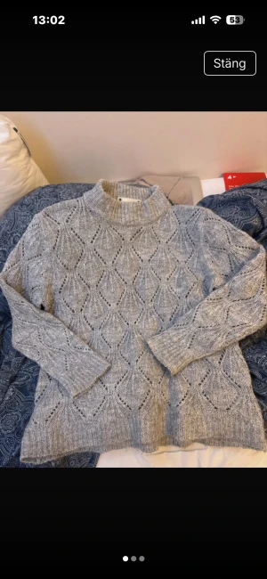 Grå stickad polotröja från Co'couture - Säljer en grå stickad polotröja från Co'couture med snyggt hålmönster i hela tröjan. Tröjan har lång ärm, ribbade muddar och hög krage som ger en chill vibe. Perfekt för dig som gillar mysiga och stilrena plagg med lite extra detaljer.