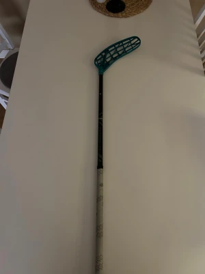 Innebandyklubba med turkos blad - Säljer en innebandyklubba med svart skaft och turkost plastblad. Klubban har grå grepp med mönster och är perfekt för dig som gillar innebandy. Bladet är det nya och är värdens lättaste. 98cm lång. Det är aldrig använt bara vinklat.