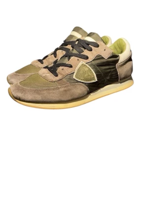 Olivgröna sneakers från Philippe Model - Snygga sneakers från Philippe Model i olivgrönt och beige med detaljer i mocka, mesh och glansigt tyg. Skorna har svarta snören, gulaktig sula och en ikonisk sköld på sidan. Perfekta för dig som gillar streetstyle och unika materialkombinationer.