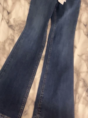 Blå bootcut jeans från Gina - Säljer ett par blå bootcut jeans från Gina. Jeans med fickor bak och dekorativa knappar.