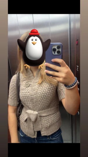 Beige stickad kofta från H&M - Snygg beige stickad kofta från H&M med korta ärmar, knytband i midjan och en stor dekorativ knapp vid kragen. Koftan har ett strukturerat stickmönster och en bred krage som ger en trendig look. Perfekt att slänga över en topp till jeans.