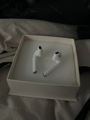 Trådlösa vita hörlurar från Apple - Snygga trådlösa hörlurar från Apple i klassisk vit färg. De har en stilren och minimalistisk design med rundade former och silverdetaljer längst ner. Perfekta för musik, poddar och samtal på språng.vet ej om dessa fungerar efter som de inte finns ett skal till 😬